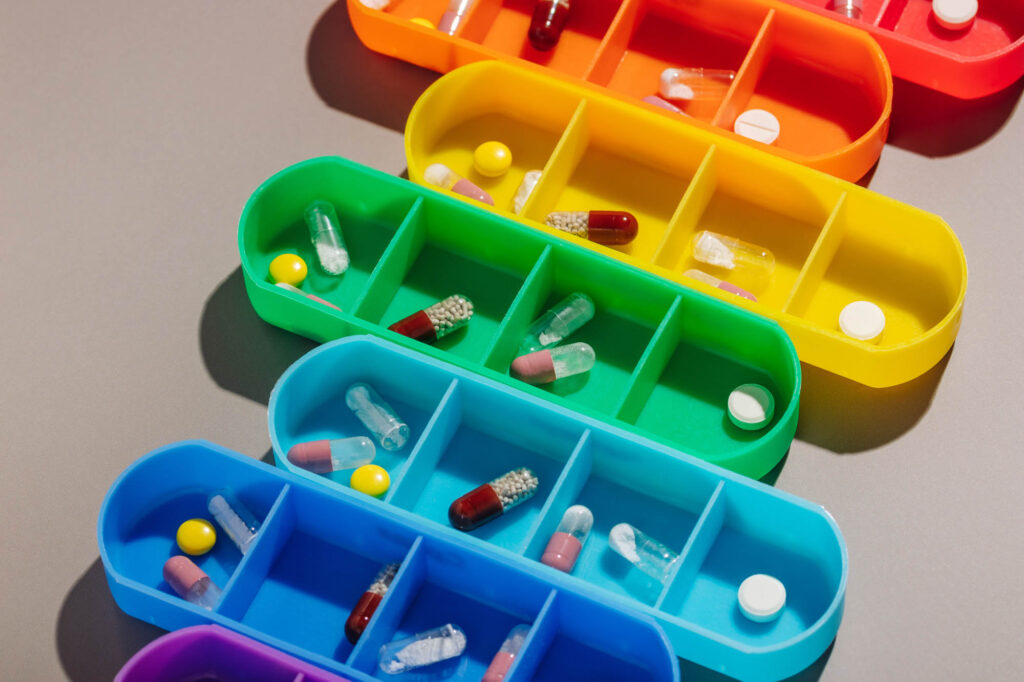 Bright multi-colored pill boxes with medicines on a gray background | Healnex